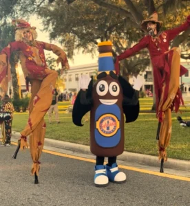 Two people on stilts dressed as scarecrows with a soda pop mascot standing in between them.